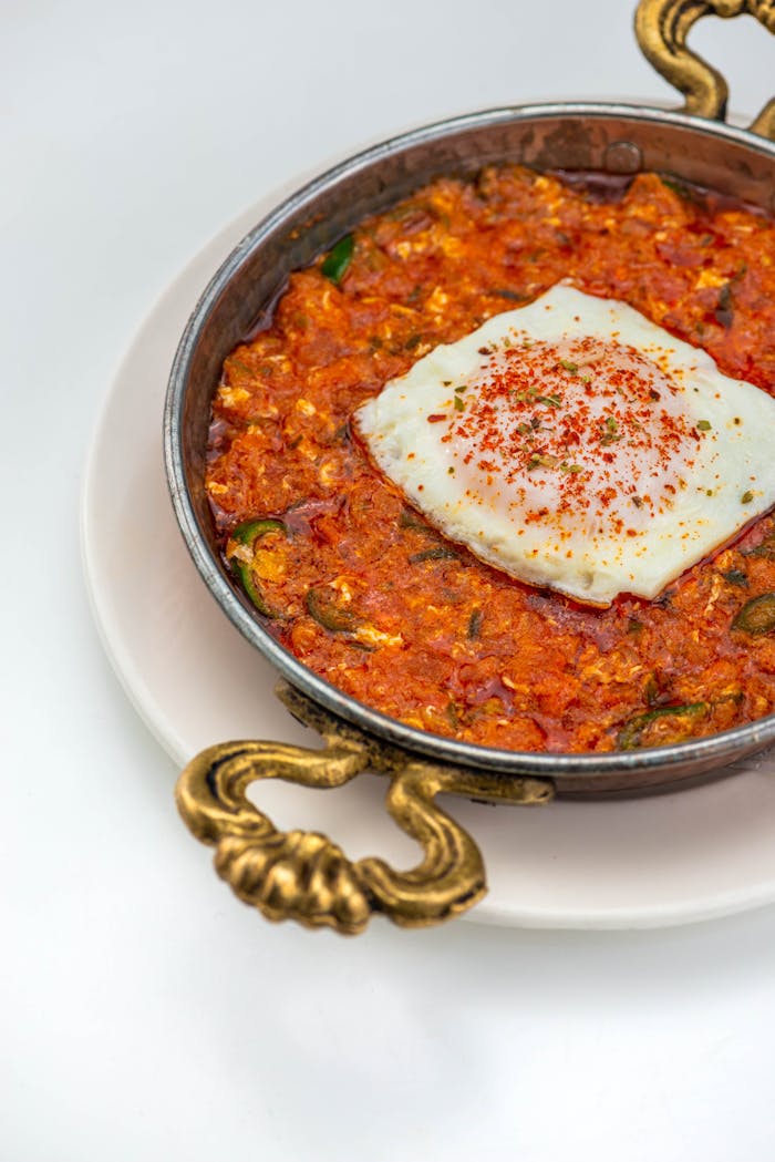 services-01 Tasty shakshuka dish with poached egg in a copper pan, garnished beautifully, served on a white plate.