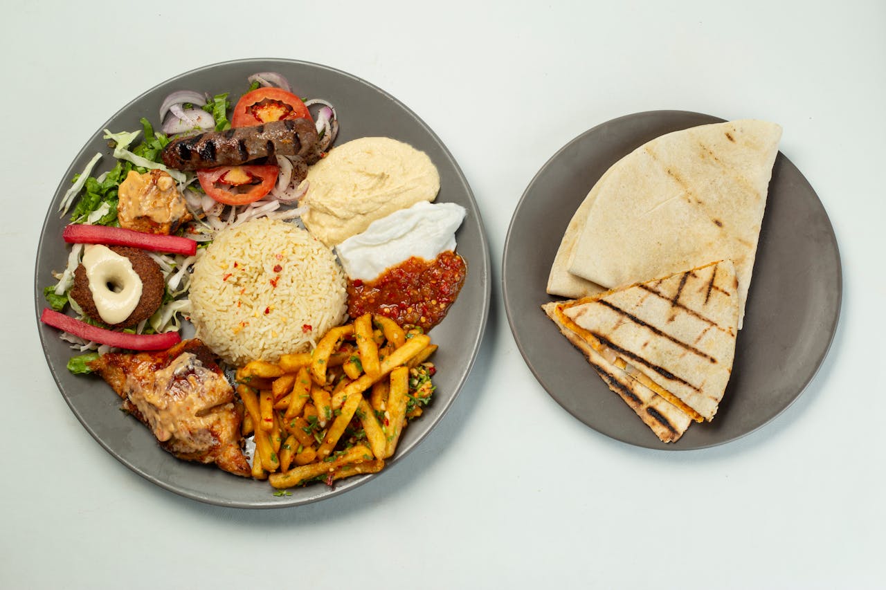 services-03 A vibrant flat lay of a Middle Eastern meal with rice, hummus, sausage, and pita bread.